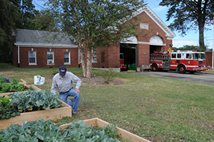 gentlemen tending to vegetable gardens outside a fire station